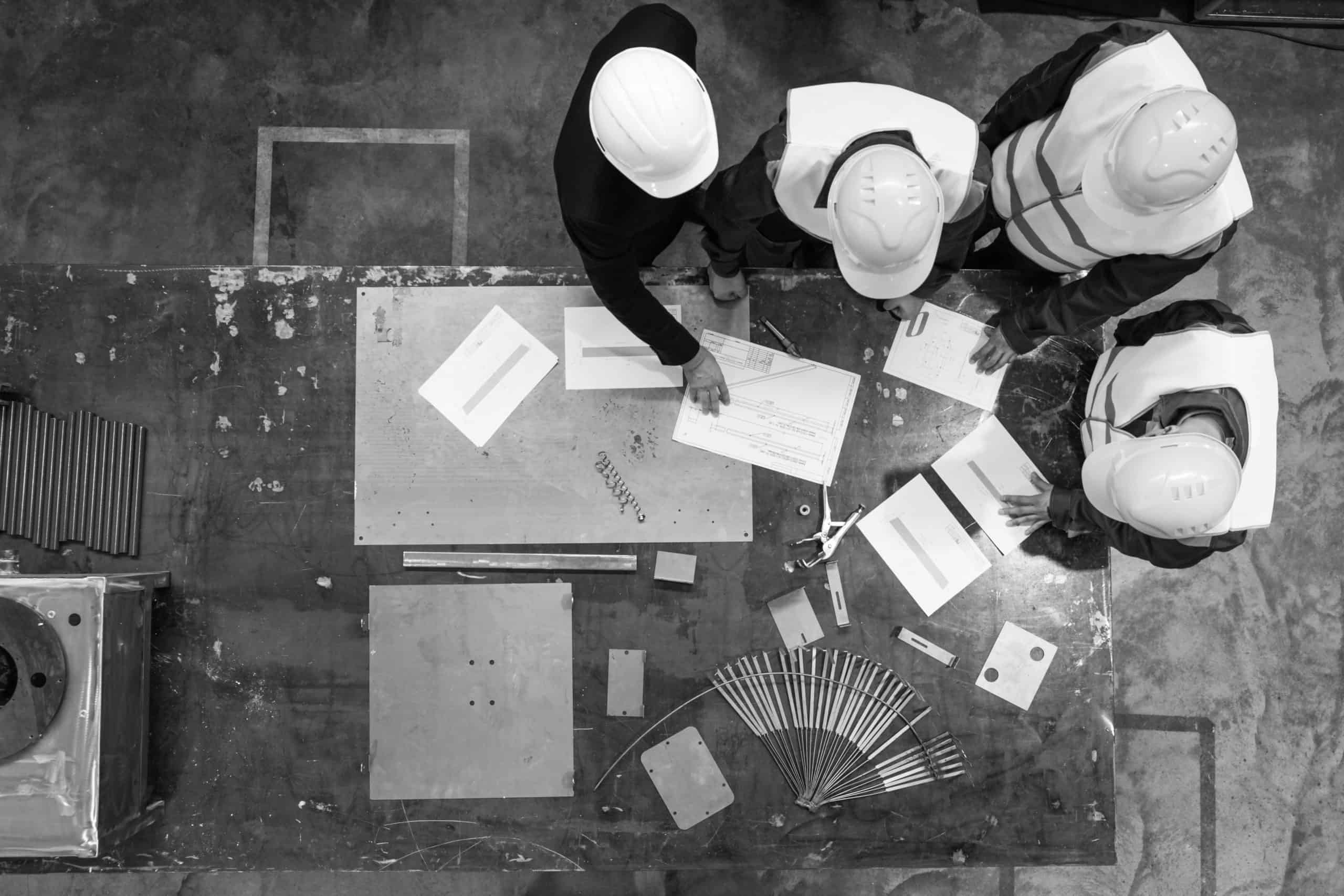 Workers and manager in safety helmets working with documents at factory table